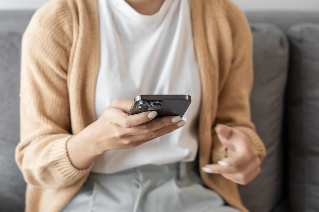 A person is at home on their couch, on their cell phone and talking with their doctor via telehealth.