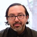 Alex Ortega Loayza, M.D., M.C.R. has slicked back dark hair, eye glasses, and wearing an orange shirt with black vest.