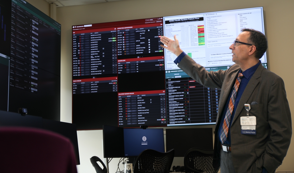 El Dr. Matthias Merkel, Ph.D., explica los datos que se muestran en el recientemente ampliado OHSU Mission Control Center. El nuevo espacio alberga el seguimiento de datos sobre el sistema de OHSU Health, capacidad hospitalaria a nivel estatal y capacidad regional en salud conductual. (OHSU/Christine Torres Hicks)