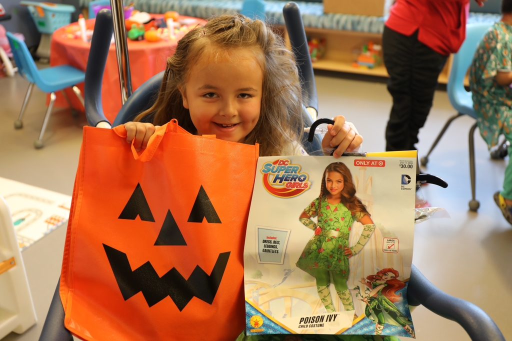 Una niña pequeña con el pelo largo y rizado rubio está sentada en una silla, sosteniendo su nuevo disfraz de Poison Ivy y sonriendo. Doernbecher de OHSU ofrece consejos de seguridad para las próximas celebraciones de Halloween. Una paciente del Doernbecher Children's hospital de OHSU muestra un disfraz y una bolsa de golosinas que recibió durante un evento de Halloween. El Doernbecher Children's Hospital de OHSU ofrece consejos para garantizar que los niños y las familias de la comunidad se diviertan de manera segura este Halloween. (OHSU/Christine Torres Hicks)