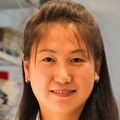 Haijiao Zhang, M.D., has long, straight, dark hair, with partially pulled back away from face. She is wearing a white lab coat and is standing near a lab bench in her lab at the Knight Cancer Institute.