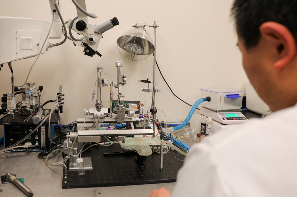 Un investigador, vestido con bata blanca y cabello corto y oscuro, trabaja en una estación de pruebas en el laboratorio Tupone de OHSU.