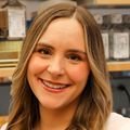 Lauren Rust, Ph.D., has long loose curly hair, parted to the side, a white tank top and smiling in the lab.