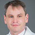 David Woodland, M.D., has short gray hair and wearing a white coat, standing against a gray background.