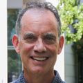 Tom Scanlan, Ph.D., in a garden at Oregon Health & Science University. He is tall, has short dark gray curly hair and smiling.