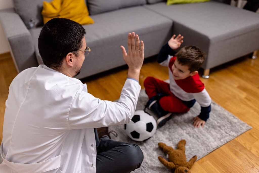 Man in white coat high-fiving child with autism