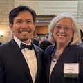 David Huang, M.D., Ph.D., left, has a black suit and bow tie and white shirt, dark hair parted to one side, light facial hair, and is smiling next to Lisa Coussens, Ph.D., who has gray cropped hair, a black sweater, white shirt, eye glasses, and a coloful necklace, smiling.