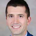 Zachary Working, M.D., has short black hair and a blue suit, smiling in a photo studio.