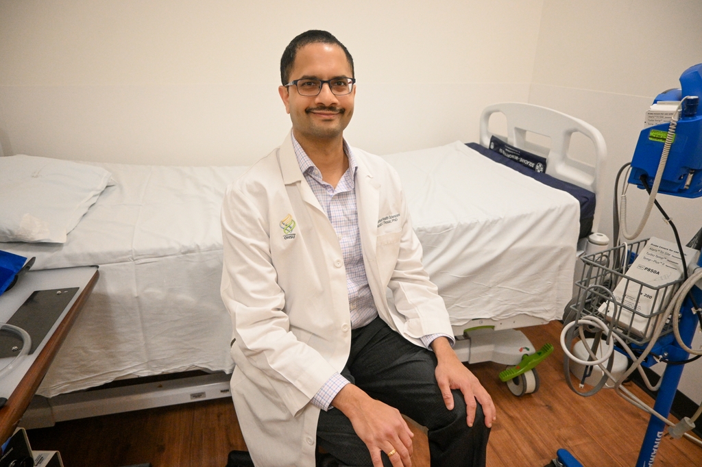 Image is of Saurabh Thosar, sitting on a stool in front of a sleep study bed and equipment.