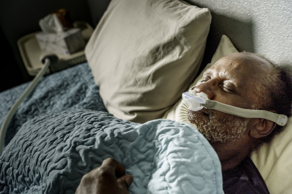Untreated sleep apnea raises risk of Parkinsons study finds: A man is in bed, sleeping with a CPAP on his face.