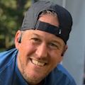 Matt Hazard has dark blond hair covered in a backward ball cap, kneeling on grass, adjusting his show, as he preps for running.