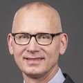 Hagen Kennecke, M.D., M.H.A., FRCPC, has no hair, eye glasses, a suit and tie, and smiling in a photo studio.