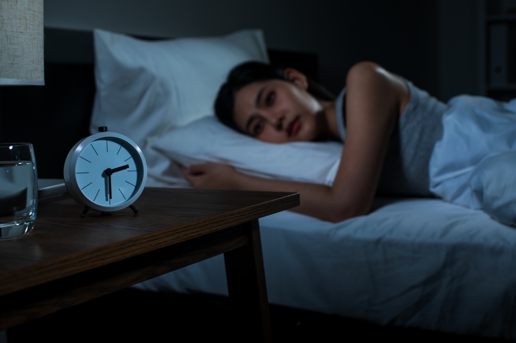 Insufficient sleep; image is of a woman laying down in bed no sleeping and looking at a clock on her nightstand.