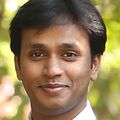 Manideep Chavali, Ph.D., has short dark hair with a side part, a suit and is smiling in a garden area.