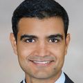 Sudhir Isharwal, M.D., has short dark hair, and a suit, smiling against a gray background