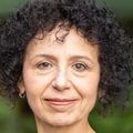 Rodica Busui, M.D., Ph.D., has short curly hair and a patterned black and white jacket, smiling in a grassy area.