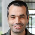 Adem Yildirim, Ph.D., tiene cabello corto negro/gris y una chaqueta gris, y sonríe en el pasillo del edificio OHSU Knight Cancer.