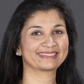 Vijayshree Yadav has log wavy black hair, a black top and smiling against a dark gray background.