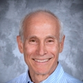 David Lieberman has sparse white hair and smiling against a gray cloud-like background.