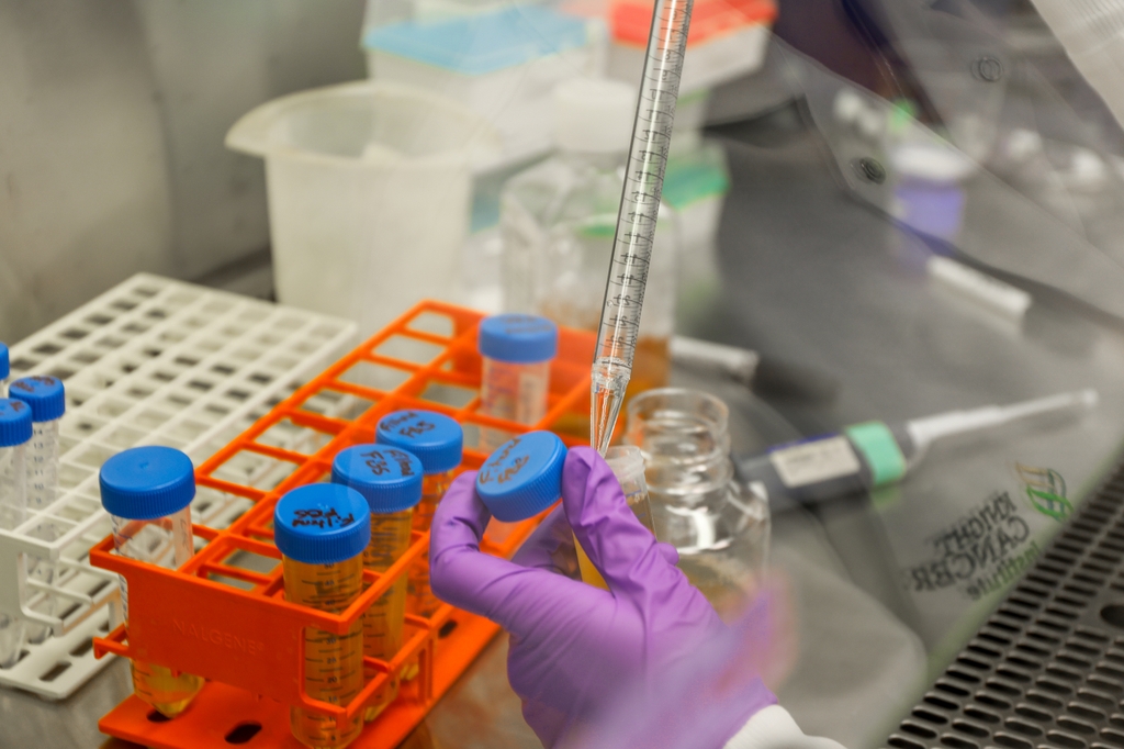 La foto muestra el guante de un trabajador de laboratorio trabajando de cerca en el llenado de tubos.