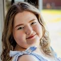 Hailey Hughes has medium-length curly blonde hair and a light blue dress.