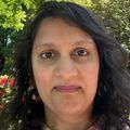 Anjali Rameshbabu, Ph.D., has long dark, wavy hair, and is standing in a garden area,