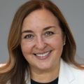 Lisa Fajardo Faust has long brown hair, a white suit and black top, smiling.