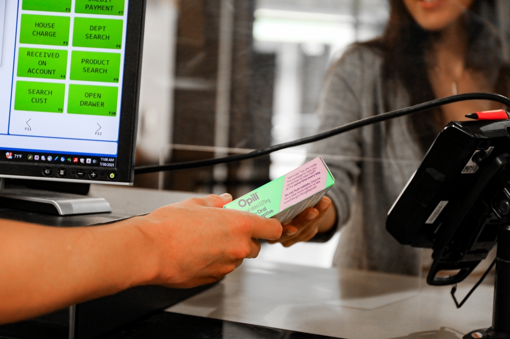 Image is of a woman with long dark hair, face unseen, purchasing birth control at the OHSU Pharmacy in Portland.