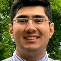 Tony Munoz has short black hair, eye glasses, and wearing a light blue shirt and tie.
