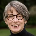 Ann Nielsen, Ph.D., RN, has cropped dark gray hair, black glasses, a black top and pearl earrings, smiling in a green area at OHSU