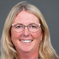 Jennifer Raybin, Ph.D., RN, CPNP, has long wavy blonde hair, eye glasses, a green leopard print top, smiling against a gray background.