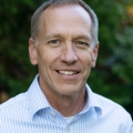 Stutzman has gray hair, light blue shirt, smiling.