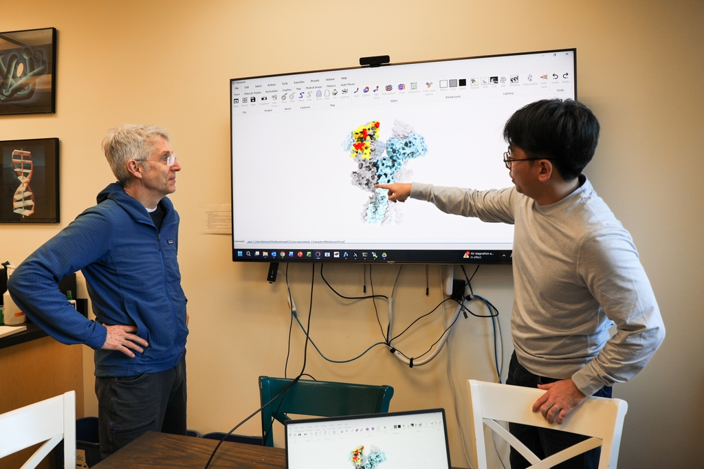 Gouaux y Kim están de pie junto a una pantalla con la imagen de un receptor.