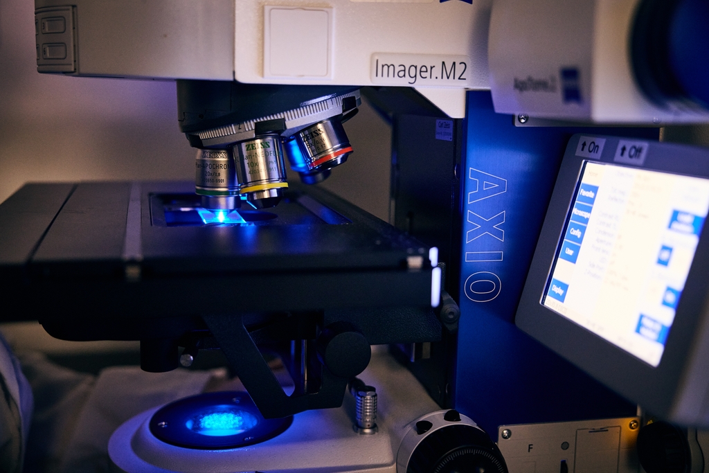 Image is of a microscope with viewing screen lighting up a darkened research lab.