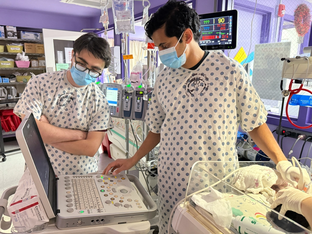 Two health care students with masks on, working in a baby unit.