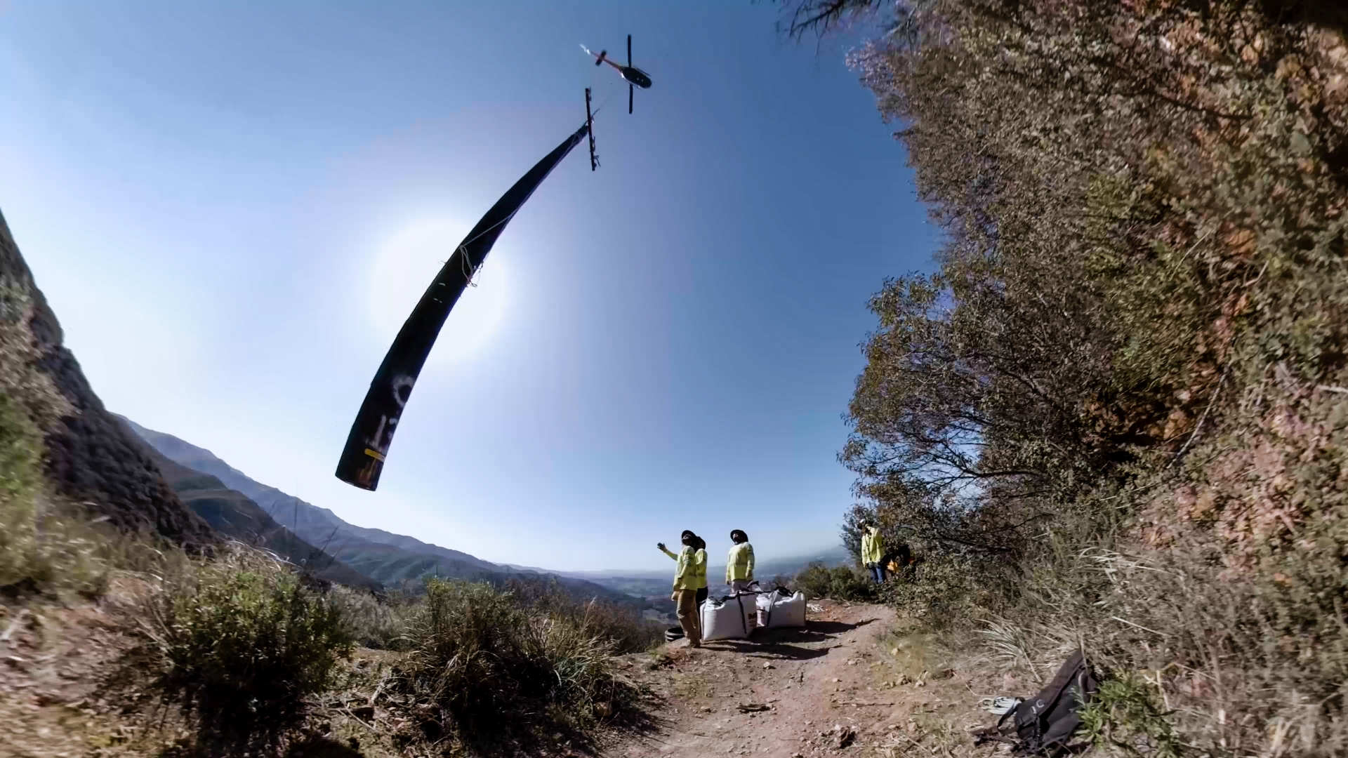 An SCE helicopter airlifts a distribution pole, which is wrapped in fire-retardant material. Linemen help guide the pole into a hand-dug hole, which they will quickly backfill with gravel once the pole is set.