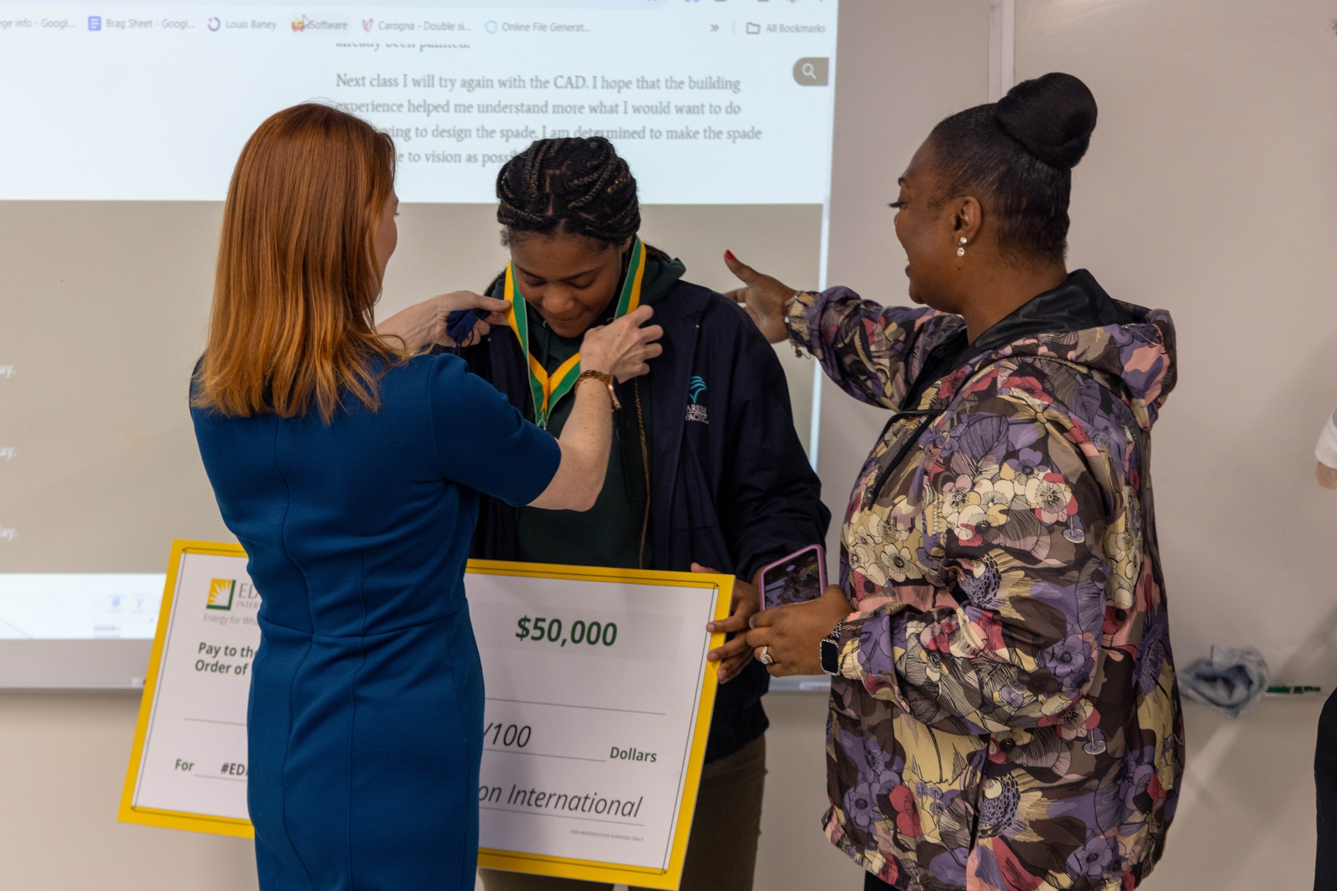 జిల్ ఆండర్సన్, SCE సీనియర్ వైస్ ప్రెసిడెంట్ మరియు చీఫ్ ఆపరేటింగ్ ఆఫీసర్, అడోనిజా తల్లి మారి పాల్ చూస్తున్నప్పుడు అడోనిజా పాల్ మెడలో ఎడిసన్ స్కాలర్ మెడల్‌ను ఉంచారు.