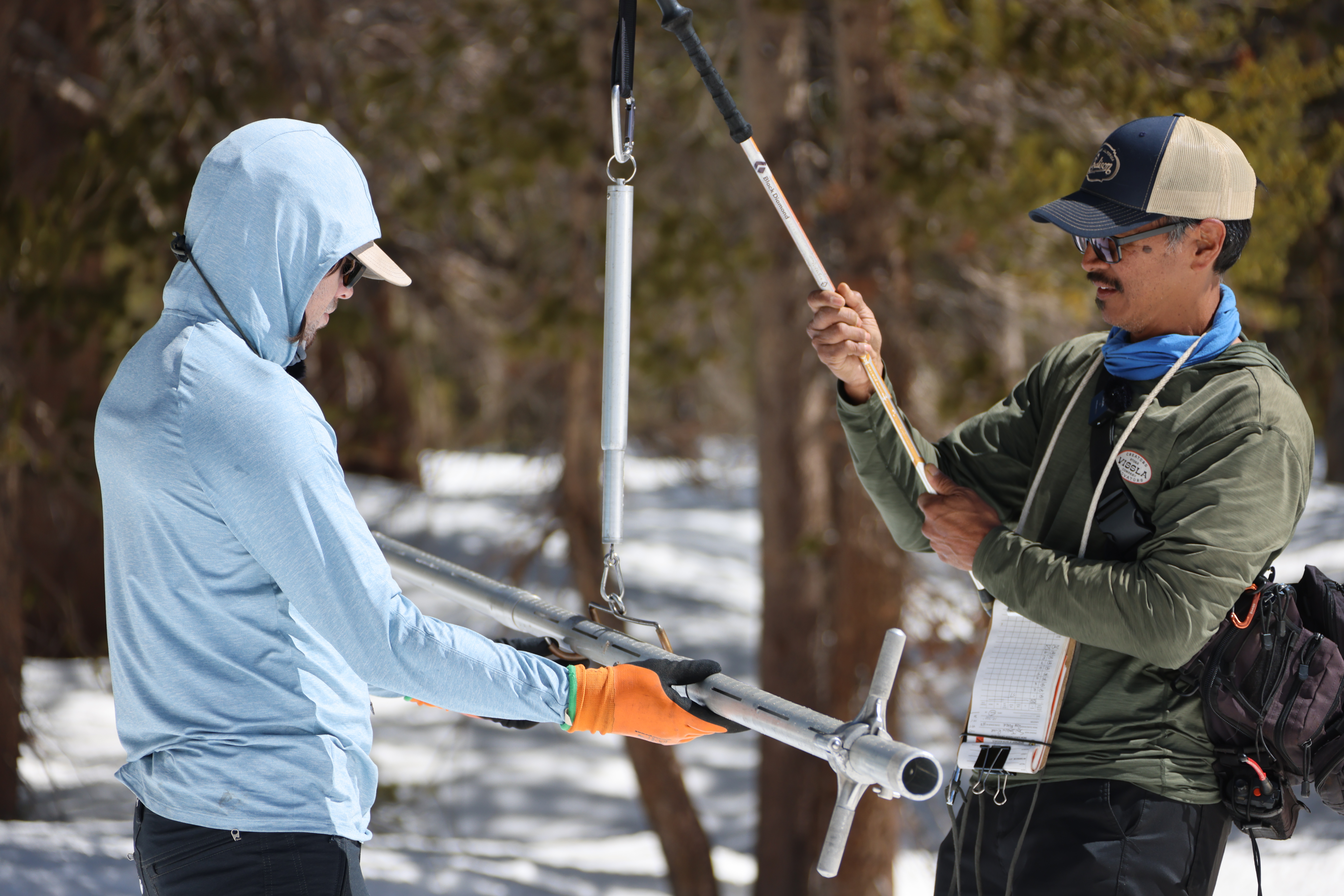 Emil Demilio (R) holds the scale tool while Michael Molina (L) balances the pole full of snow between the hooks to determine the snow's weight. 