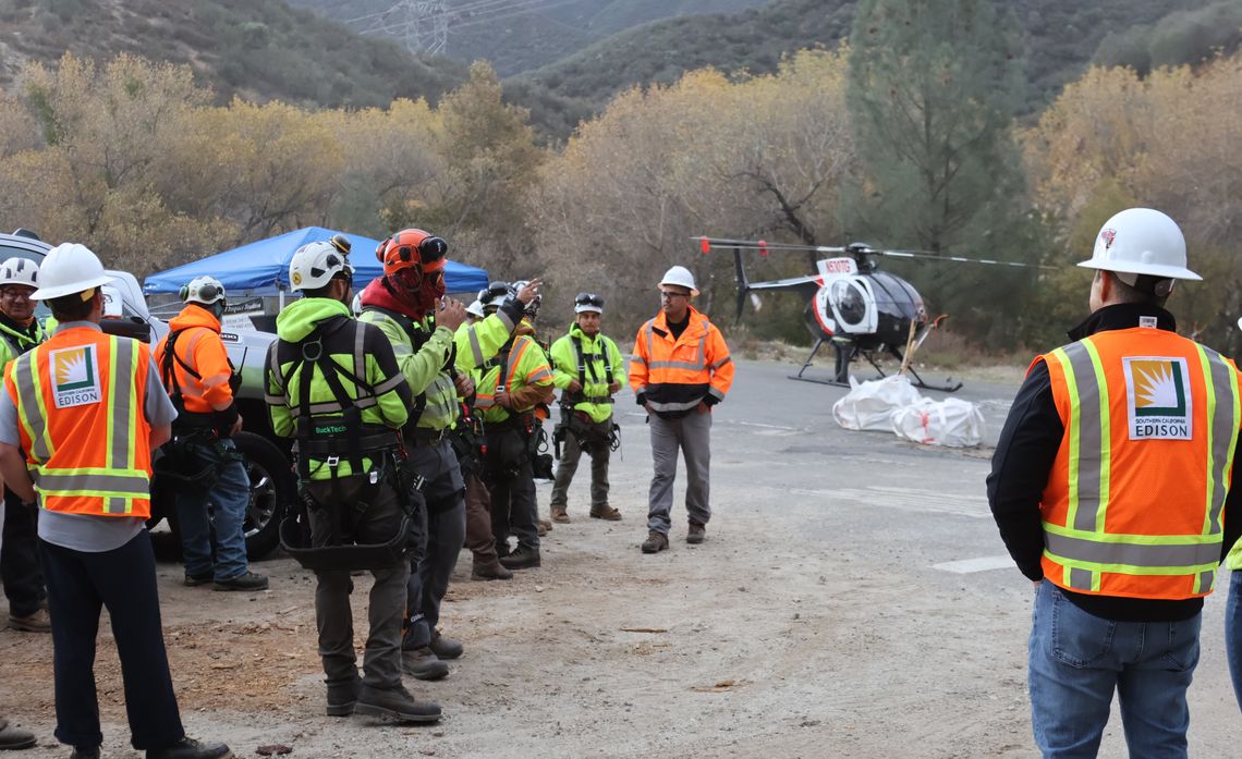 Vegetation specialists huddle in front of a helicopter to be briefed for human external cargo flights into steep, high fire risk terrain.                 