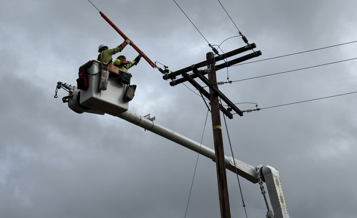 Lineman Robert Mendez and electrical crew foreman James Volinski work on a nearby utility pole, just yards from where their crew first discovered a crashed driver.