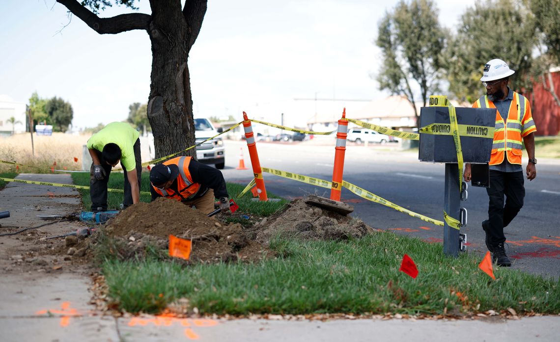 Contractors carefully dig around color‑coded markings that show where underground utility lines are located.