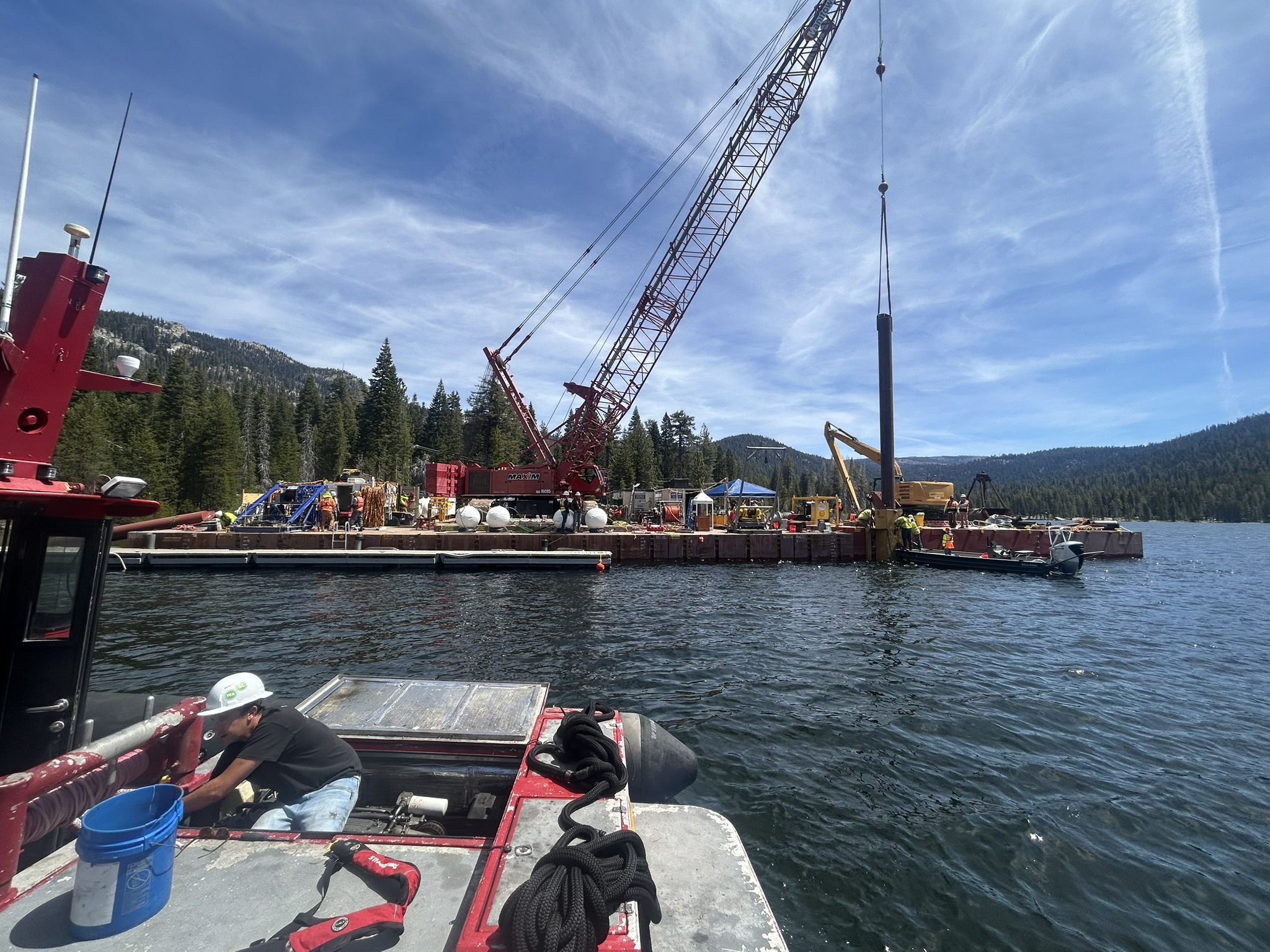 Specially-trained divers perform underwater repairs while a crane mounted on a floating barge dredges sediment from the bottom of the lake. 