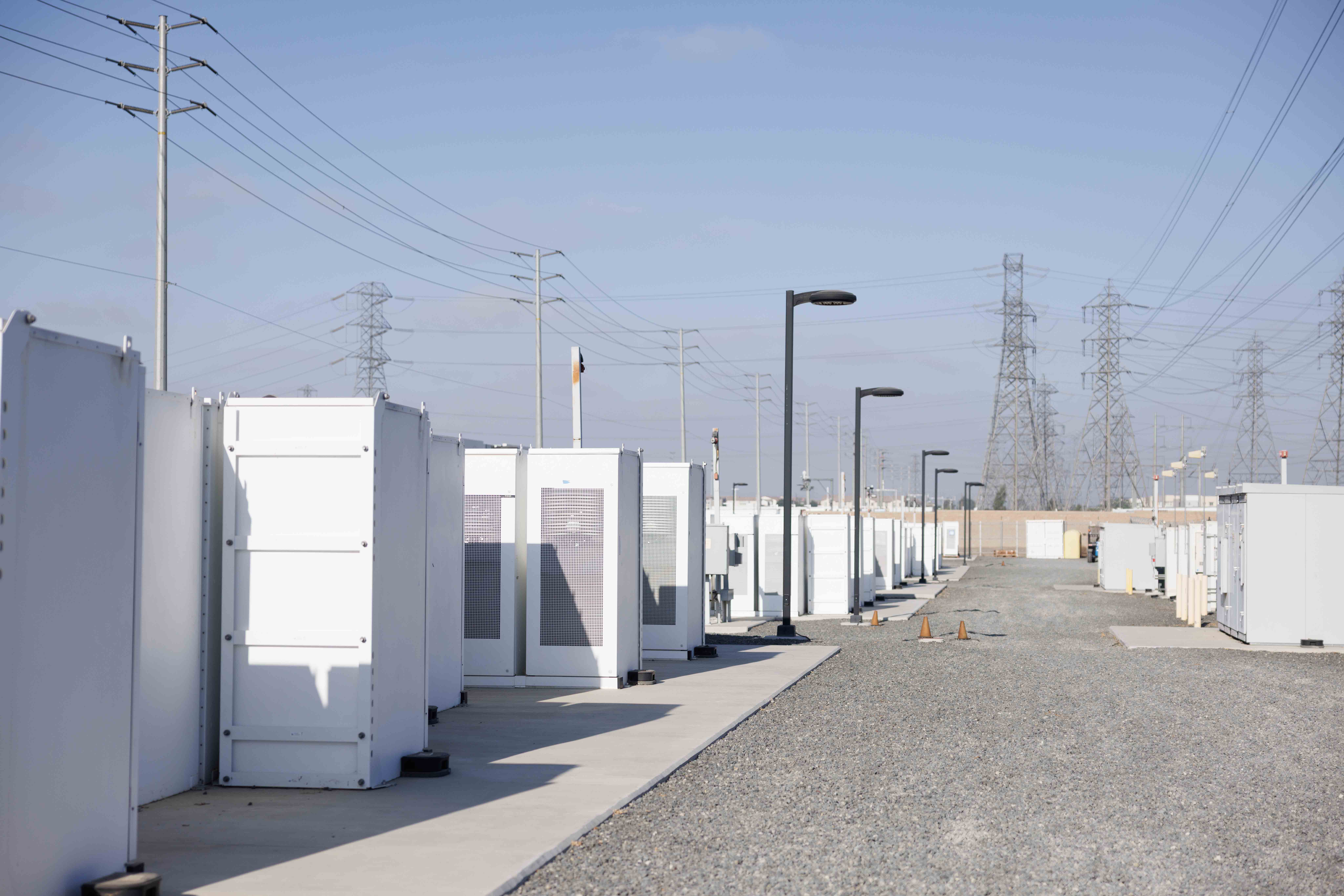 Rows of white industrial containers and tall power lines under a clear sky.