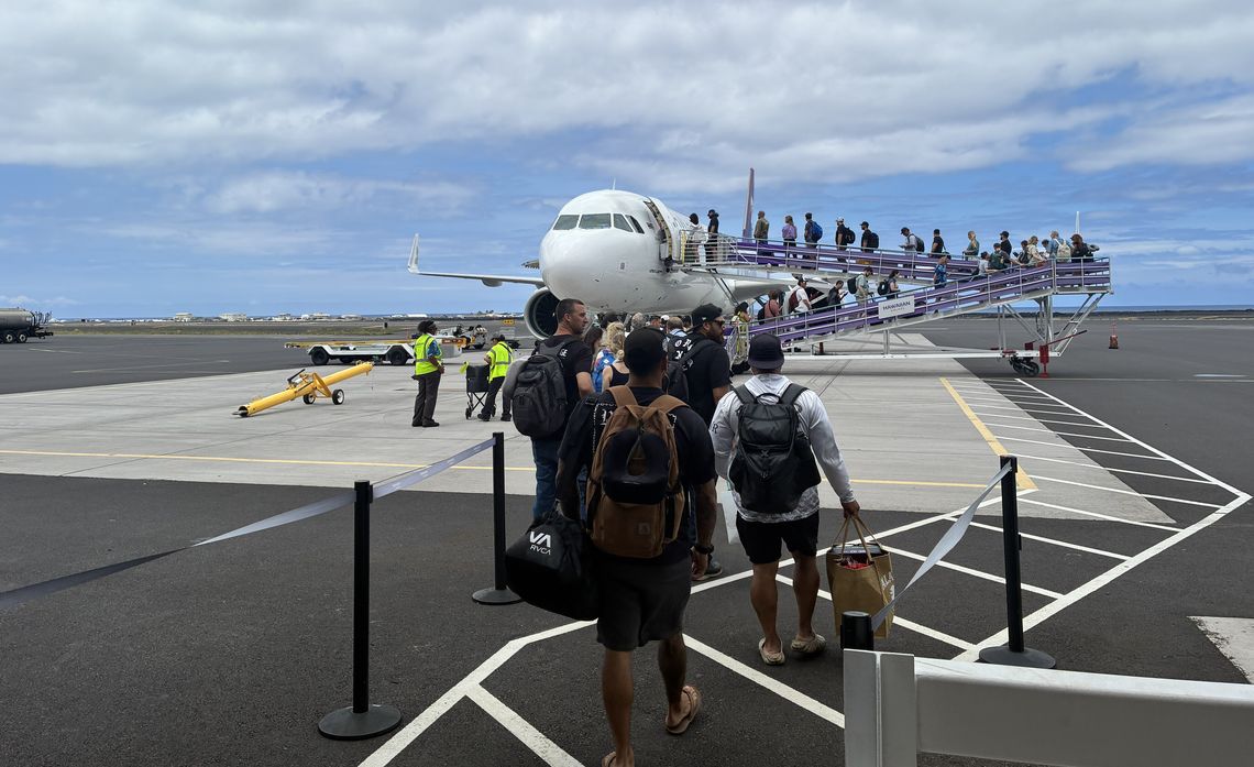 Passengers board a stationary airplane via outdoor stairs under a cloudy sky.