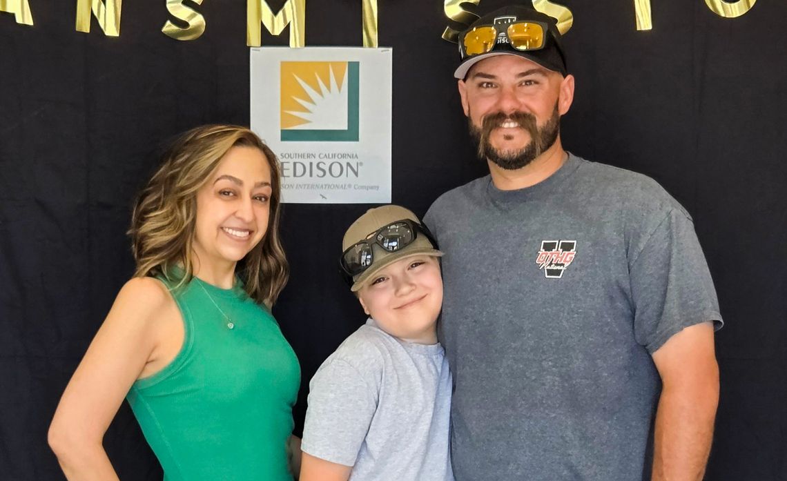 A woman in a green dress, a child wearing a cap, and a man in a gray t-shirt are smiling in front of a black backdrop with gold lettering and a Southern California Edison logo.