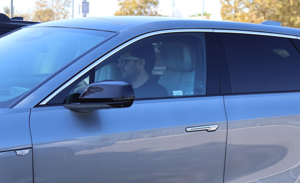 A man wearing glasses sits in the driver’s seat of a metallic blue SUV.