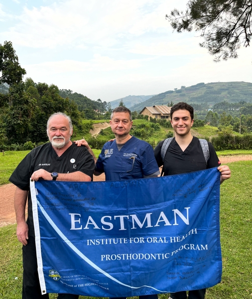 Three dentists/alumni holding the Eastman Institute for Oral Health flag