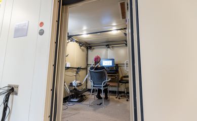 EEG booth with participant inside wearing red cap and looking at computer screen.