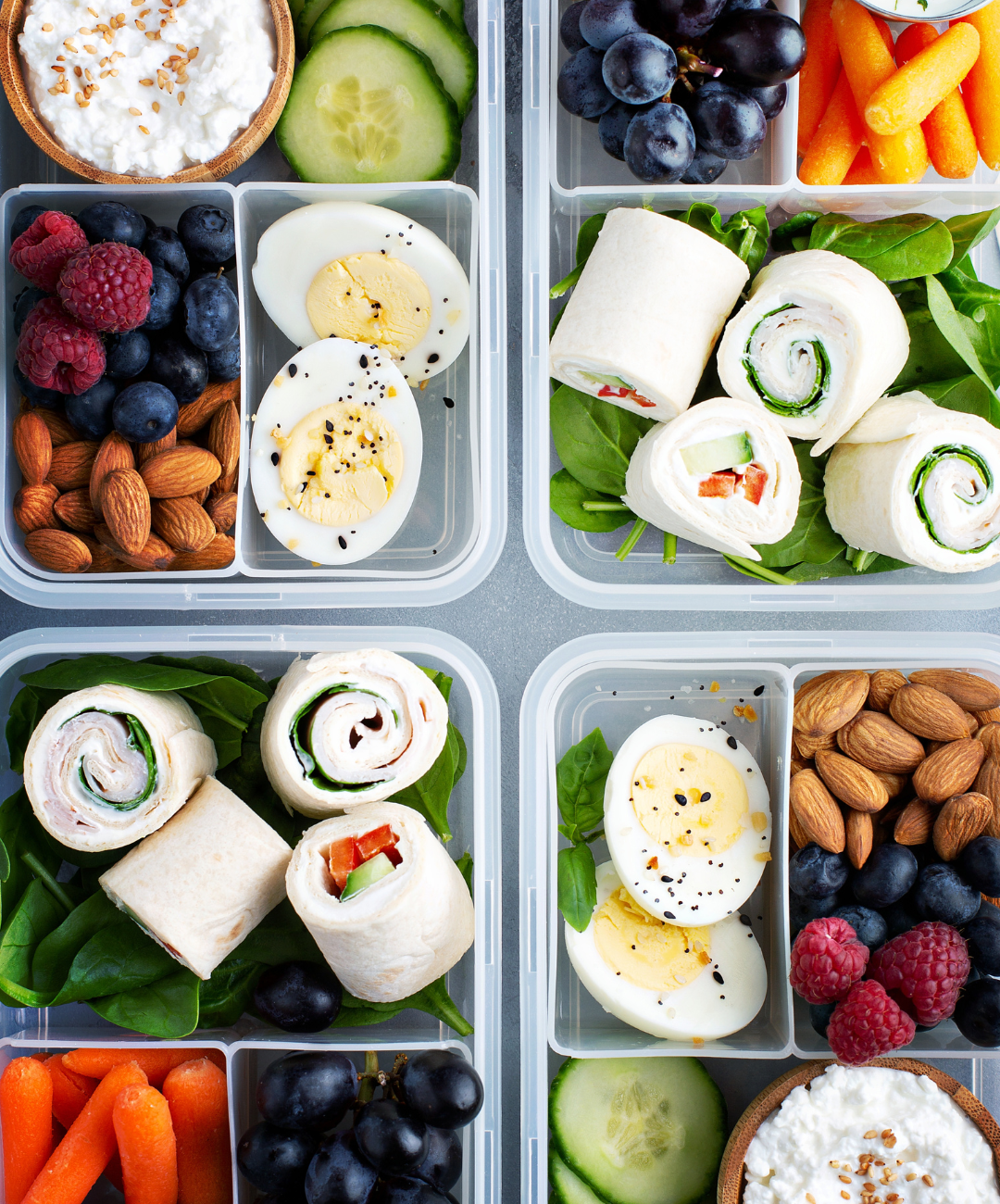 Healthy snacks in containers, including hard boiled eggs, carrots, berries, nuts, cucumbers, spinach.