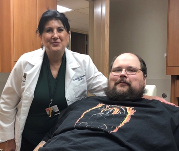A dentist in a white coat stands next to a bariatric patient who is leaned back in a dental chair.